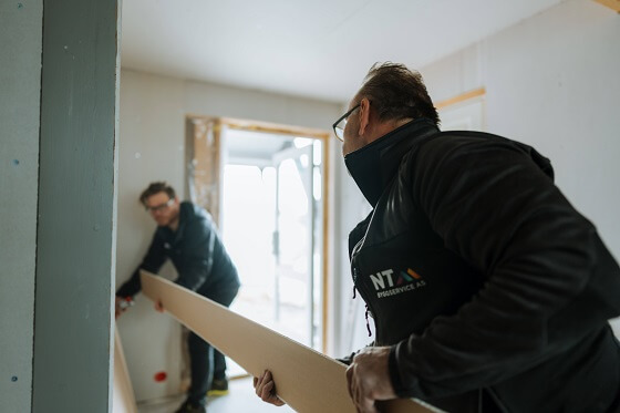 To menn som arbeider med en vegg innendørs.