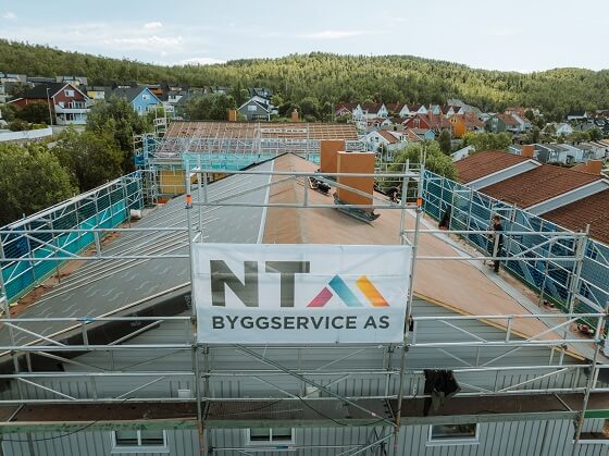 Taket på en bygning arbeides med. Bygningen har en plakat med NT Byggserivce AS logo.